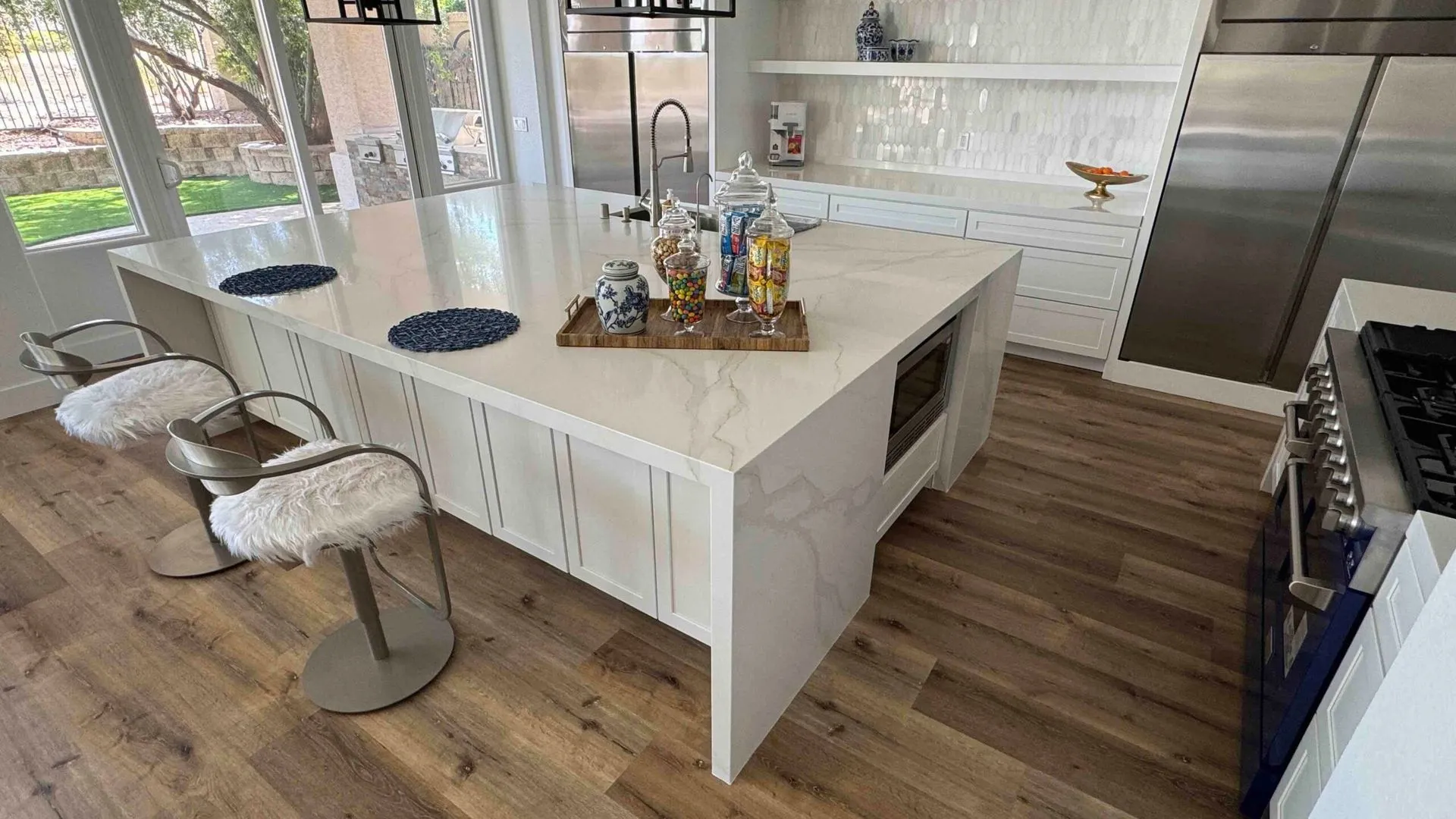 Modern Las Vegas kitchen with a white Calacatta marble waterfall island, backsplash, and warm wood cabinetry