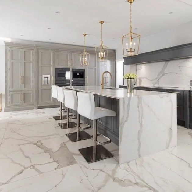 Modern kitchen featuring a sleek marble island, elegant gray cabinetry, white bar stools, and stylish pendant lighting.